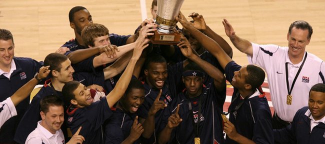 The USA team celebrates its championship victory over Greece. Taylor, the only player wearing a headband, is holding the trophy with his left hand in the front row.